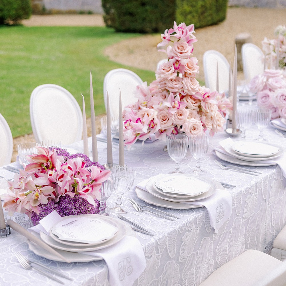 Spitzen-Overlay-Tischdecke Undine | Festtafel Outdoor Rosa Graue Spitzen-Overlay-Tischdecke mit weißer Ginkgoblatt-Stickerei auf gedecktem Hochzeitstisch im Freien, rosa Orchideen- und Liliengestecke, silbernes Besteck und Kristallgläser, Schlosspark