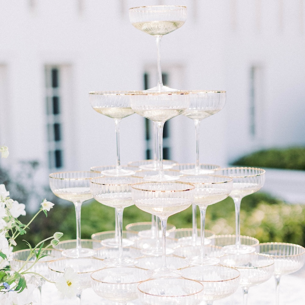 Champagnerpyramide mieten – Luxuriöse Präsentation für exklusive Feiern Eine mehrstufige Champagnerpyramide aus eleganten Sektschalen mit Goldrand, aufgestellt in einer stilvollen Outdoor-Location. Jetzt für Dein Event mieten!