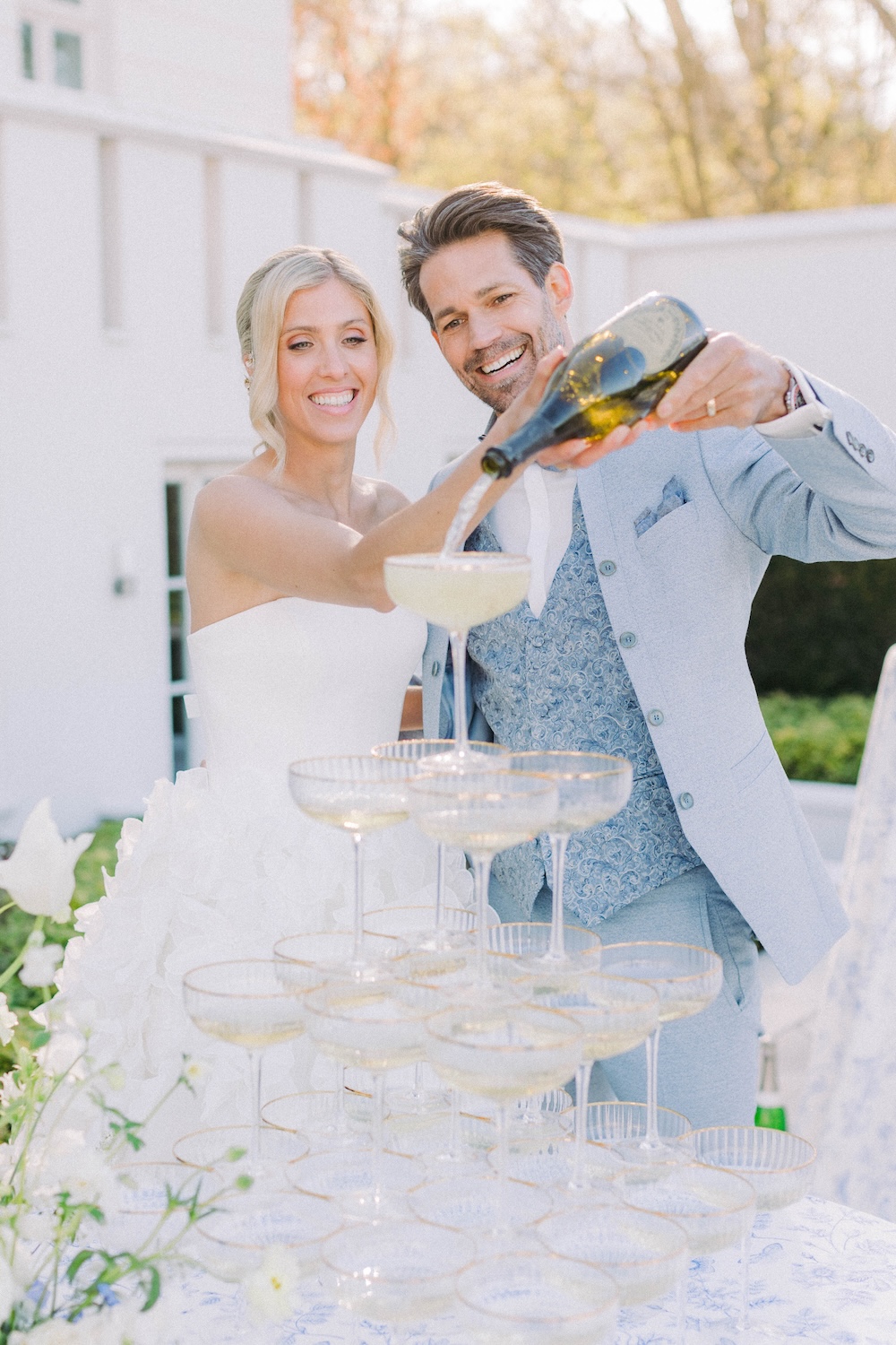 Ein glückliches Hochzeitspaar gießt Champagner in die oberste Sektschale einer eleganten Pyramide. Erlebe dieses Highlight und miete Deine eigene Champagnerpyramide! Falls du noch Anpassungen möchtest, lass es mich wissen!