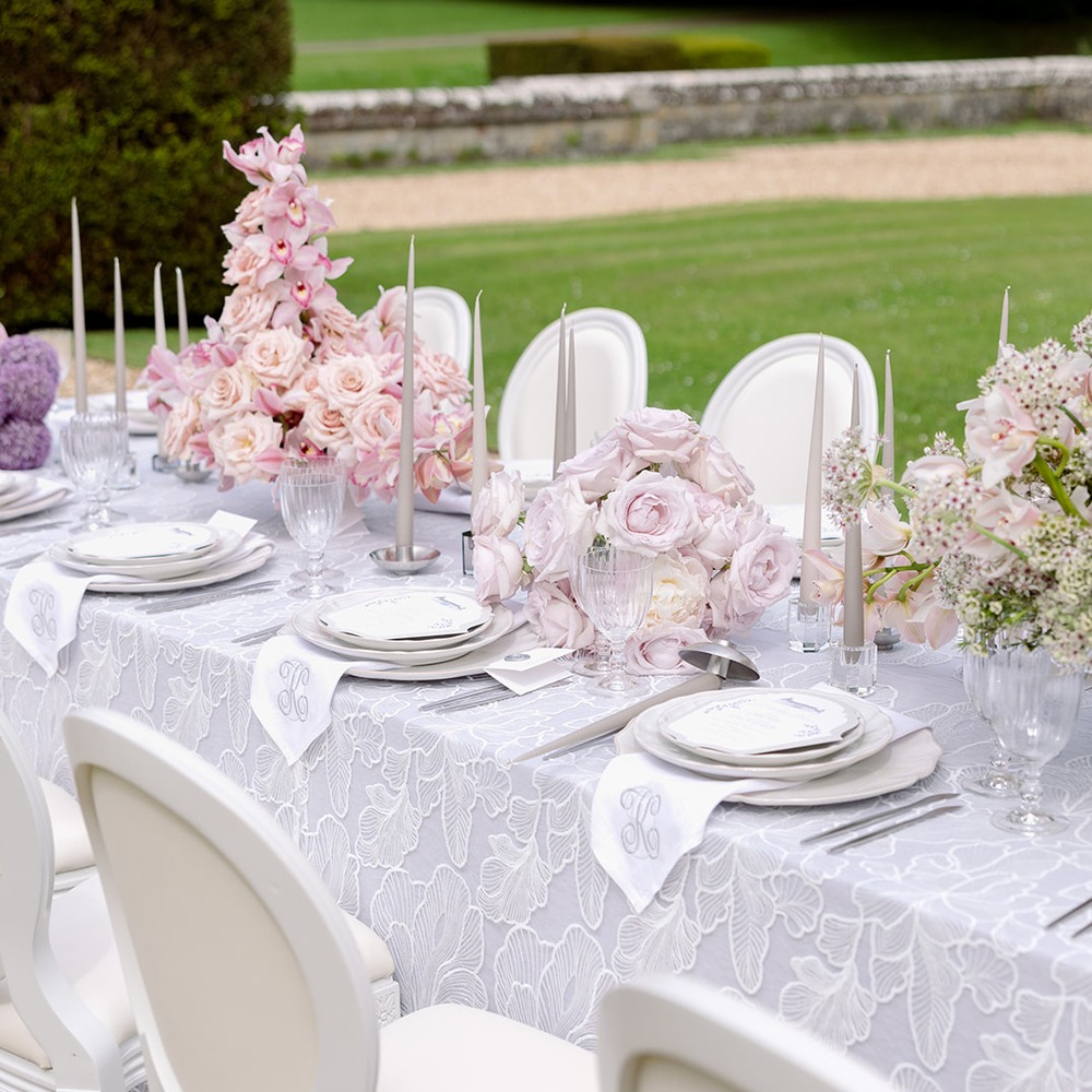 Spitzen-Overlay-Tischdecke Undine | Outdoor-Hochzeit Schlossgarten Graue Spitzen-Overlay-Tischdecke mit weißer Ginkgoblatt-Stickerei auf langem Hochzeitstisch, rosa Orchideen- und Rosengestecke, monogrammierte Leinenservietten, silberne Kerzenständer, Schlossgarten